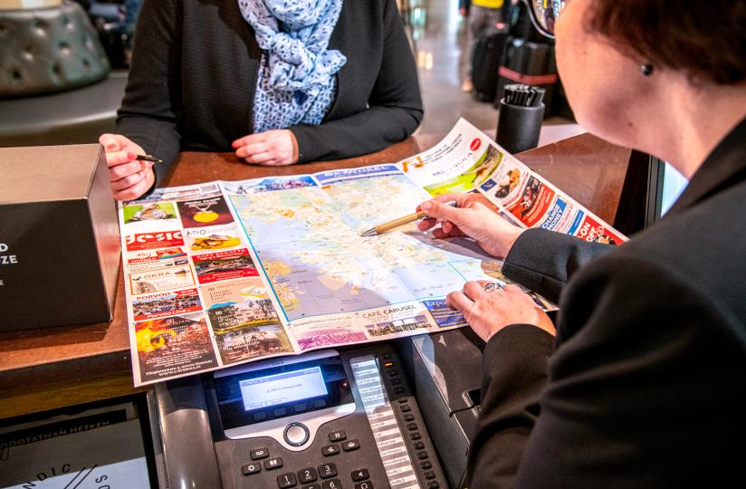 Hotellinvastaanottovirkailija näyttää asiakkaalle kartalta kohdetta.