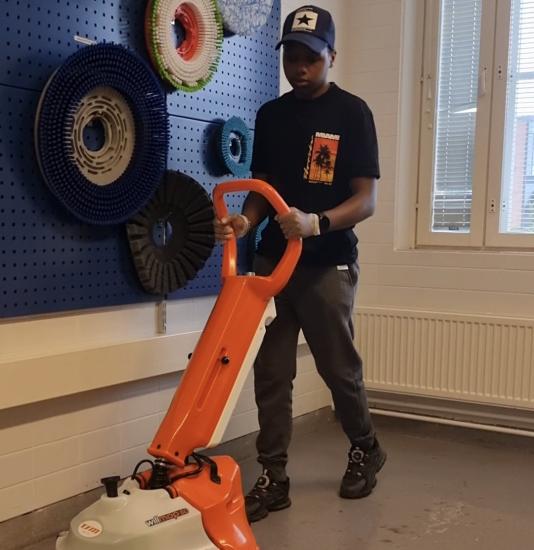 Levis Kahia työntää lattiapesuria. Taustalla näkyy erikokoisia pyöreitä harjoja.
