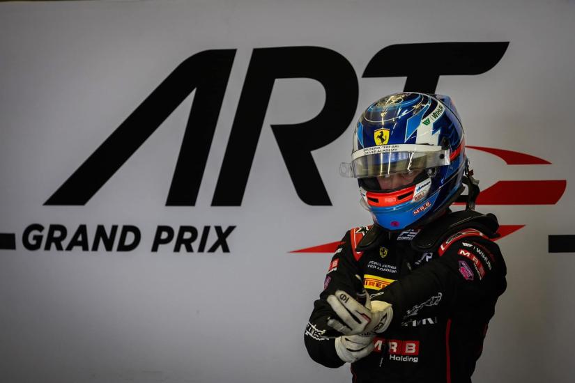 Kilpa-ajaja Tuukka Taponen seisoo ajovarusteissa ART Grand Prix -tallin varikolla, Ferrari Driver Academy -logo näkyy kypärässä.