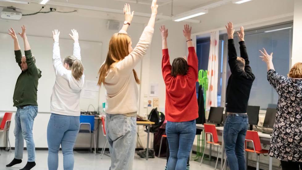 Tunnilla olevia opiskelijoita, jotka seisovat ja pitävät käsiä ylhäällä.
